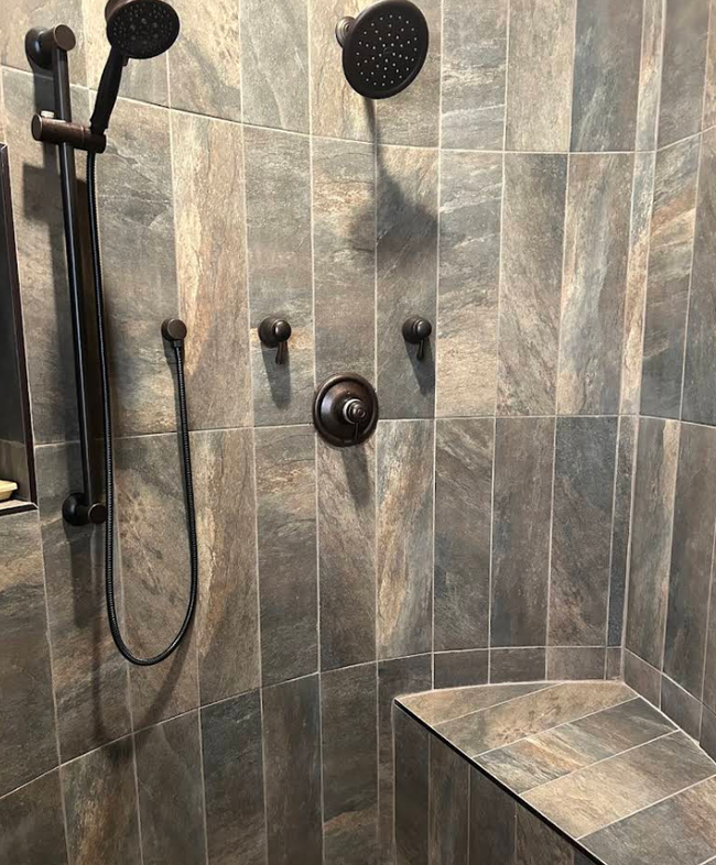 Modern tiled shower with black showerhead, handheld wand, and built-in bench.