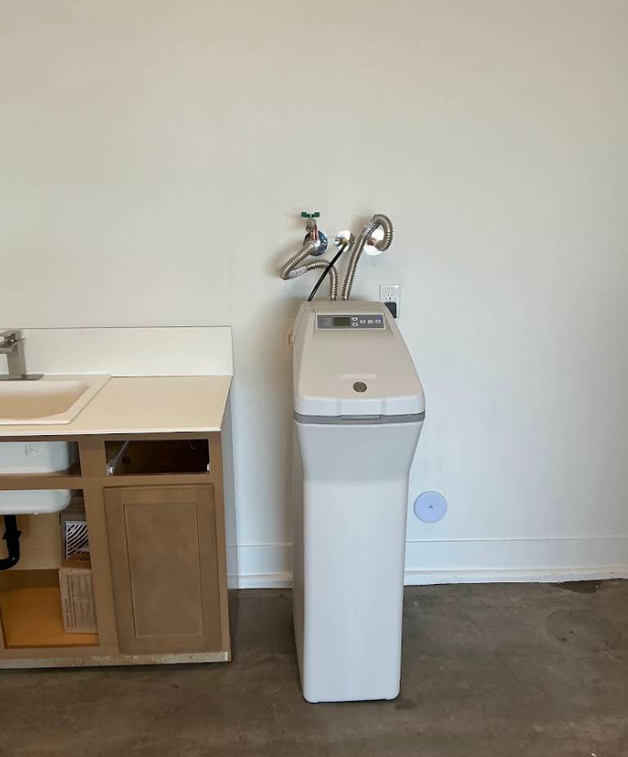 White water dispenser next to a bathroom sink vanity against a plain wall.