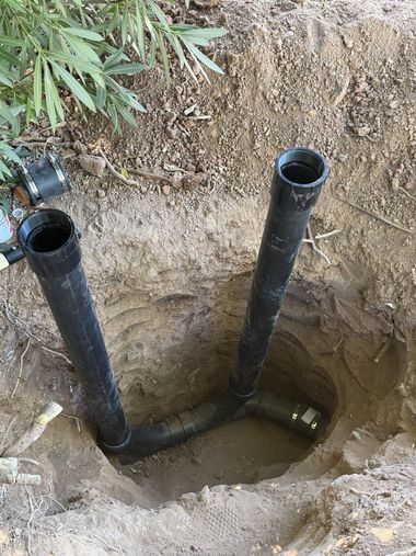 Two black pipes protrude from a dirt pit beside a small trench and exposed soil.