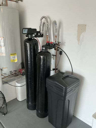 Water softener and filtration tanks beside a water heater in a utility room.