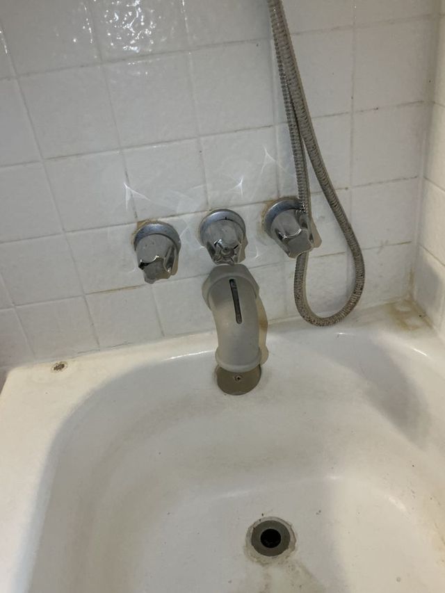 Small bathtub with a faucet and shower hose against white tiled bathroom walls.