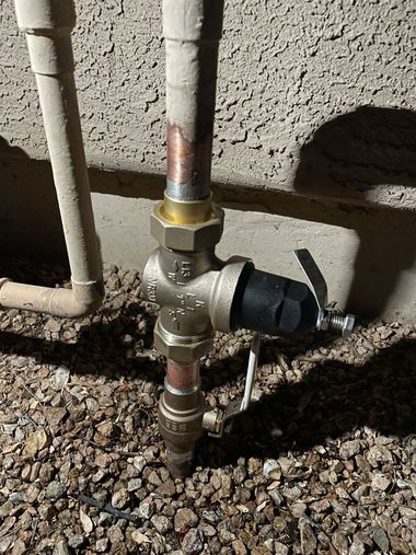 Outdoor gas pipe and valve assembly beside a stucco wall, with a black shutoff cap and gravel ground.