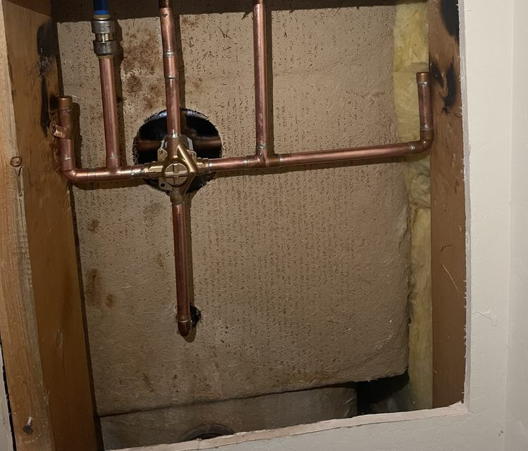 Copper plumbing pipes inside an unfinished wall opening with a circular fixture behind them.