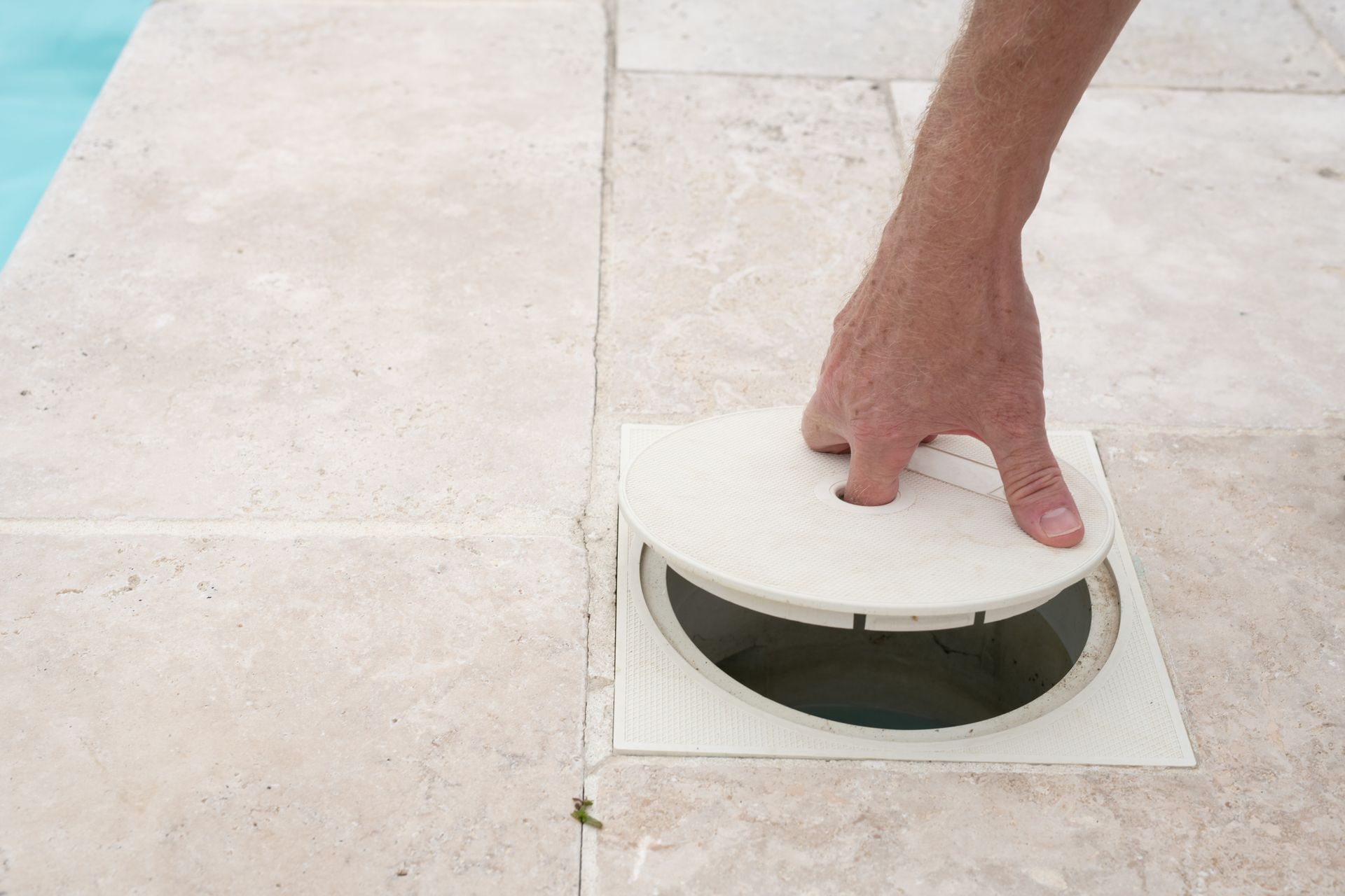 A person is opening a drain on the side of a pool.