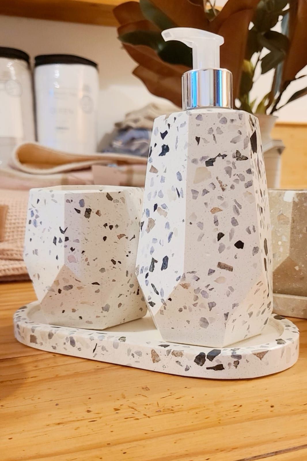 Dispensador de jabón blanco moteado y taza sobre una bandeja a juego en una mesa de madera.