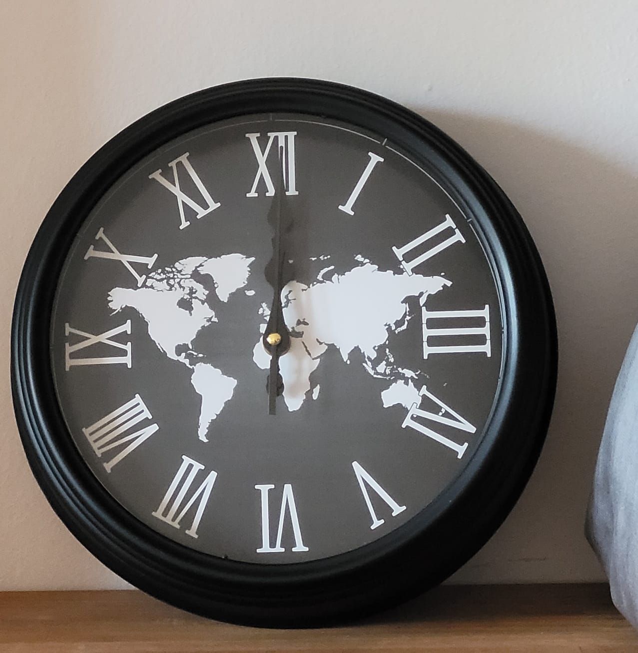 Reloj de pared negro con números romanos blancos y un diseño de mapamundi en la esfera.