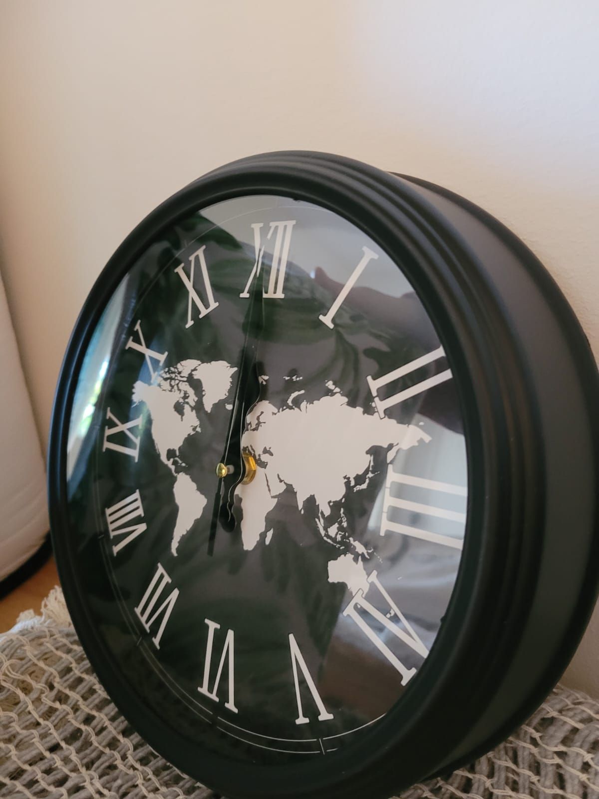 Reloj de pared negro con números romanos blancos y un diseño de mapamundi en la esfera.