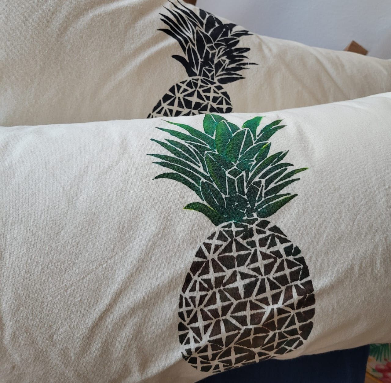 Una mano sostiene dos almohadas color crema con estampados de hojas verdes sobre un fondo claro.