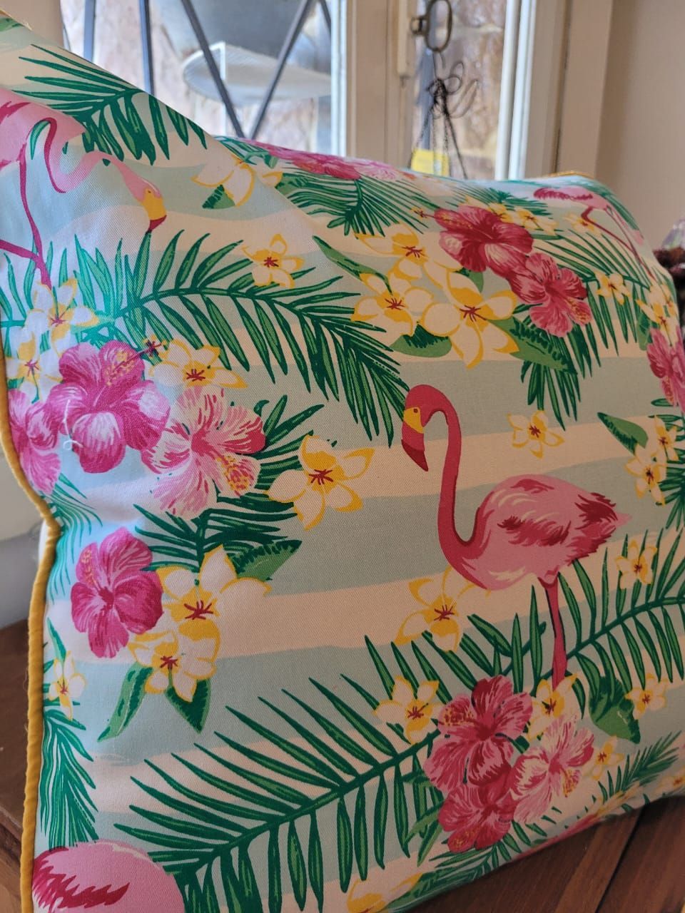 Mano sosteniendo una bolsa acolchada con estampado floral tropical, flamencos rosas y hojas verdes.