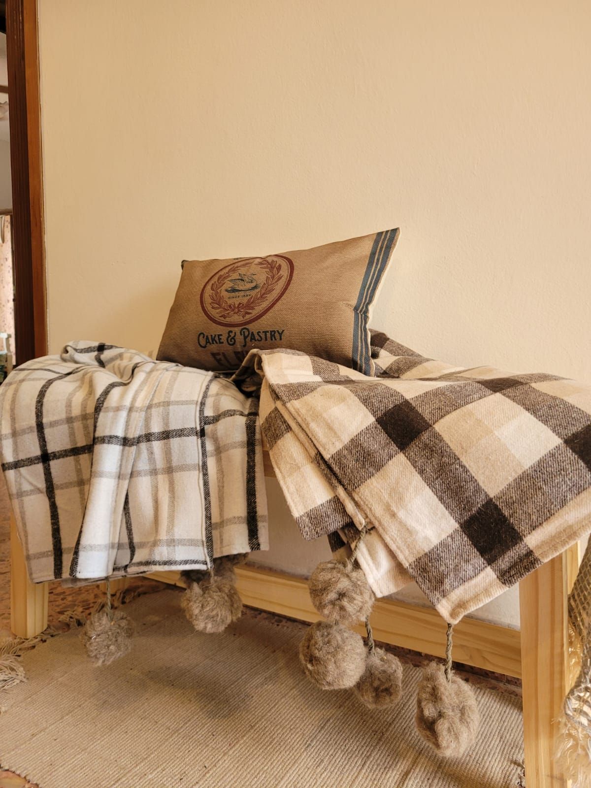 Mantas a cuadros extendidas sobre un banco de madera con un cojín decorativo en una habitación acogedora.