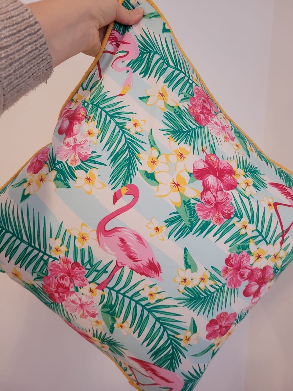 Mano sosteniendo una bolsa acolchada con estampado floral tropical, flamencos rosas y hojas verdes.
