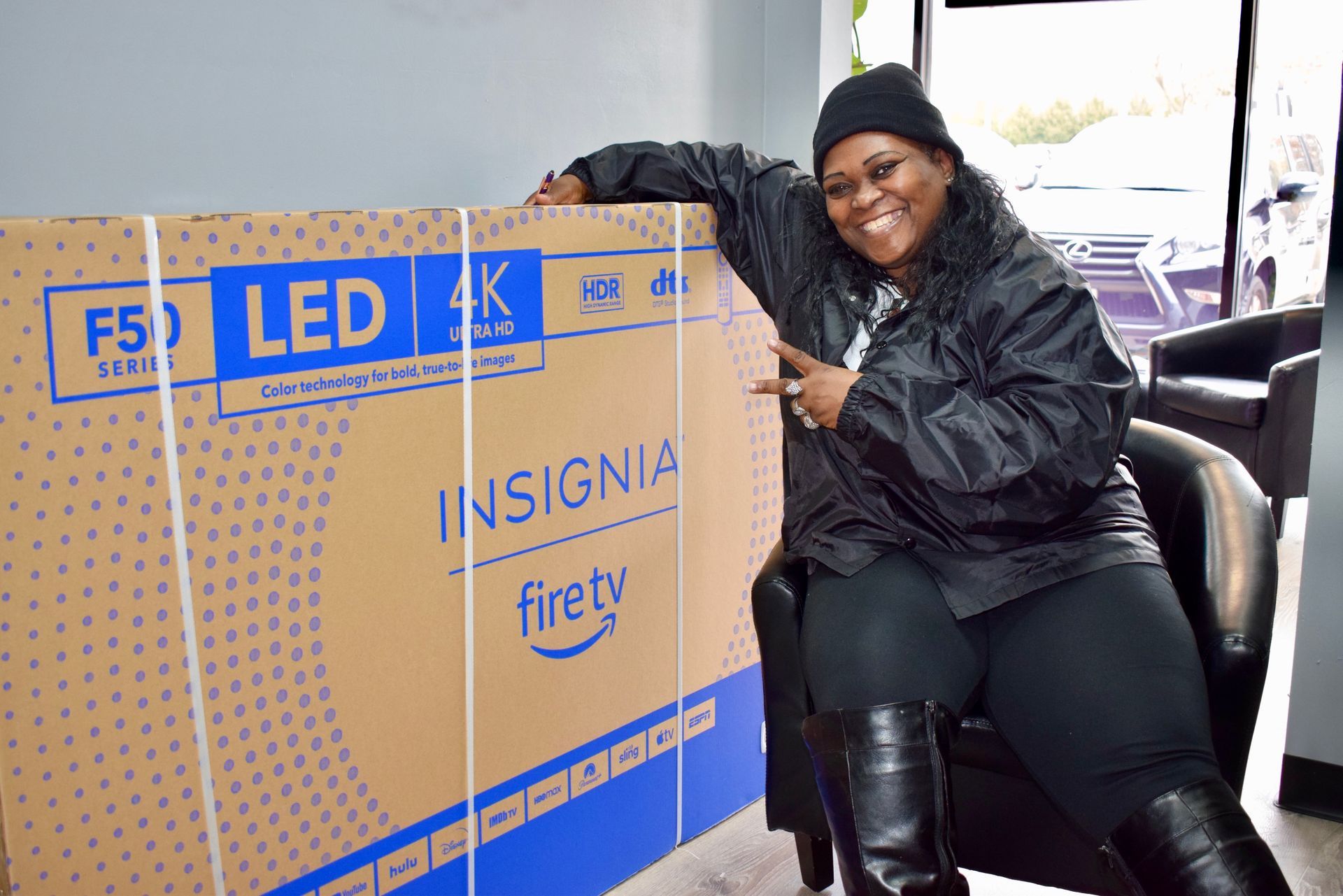 Woman smiling beside a large Insignia 50-inch 4K LED TV box in a store.