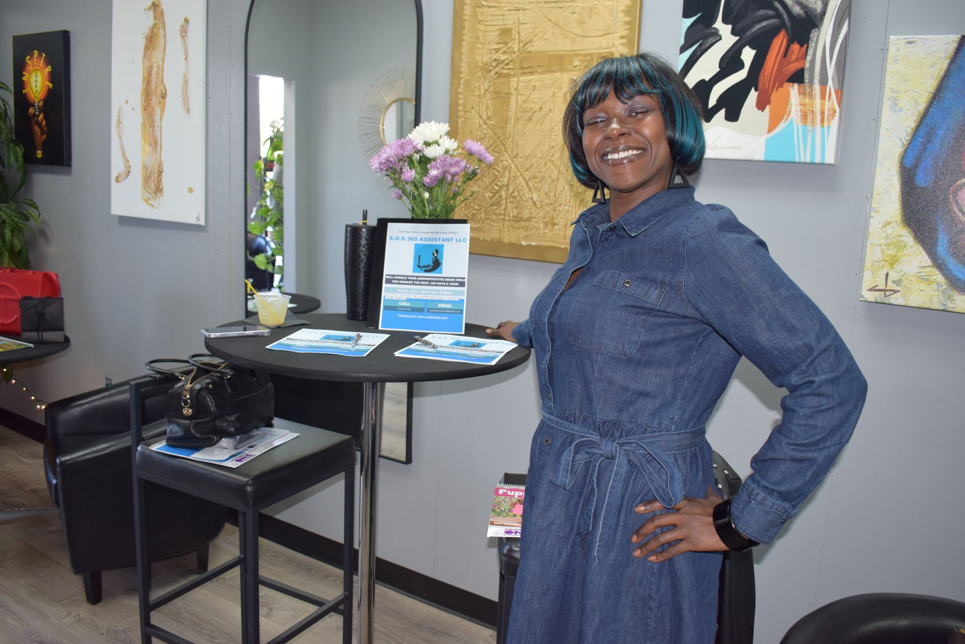 Woman smiling in a gallery-like room beside a display table with artwork on the walls.