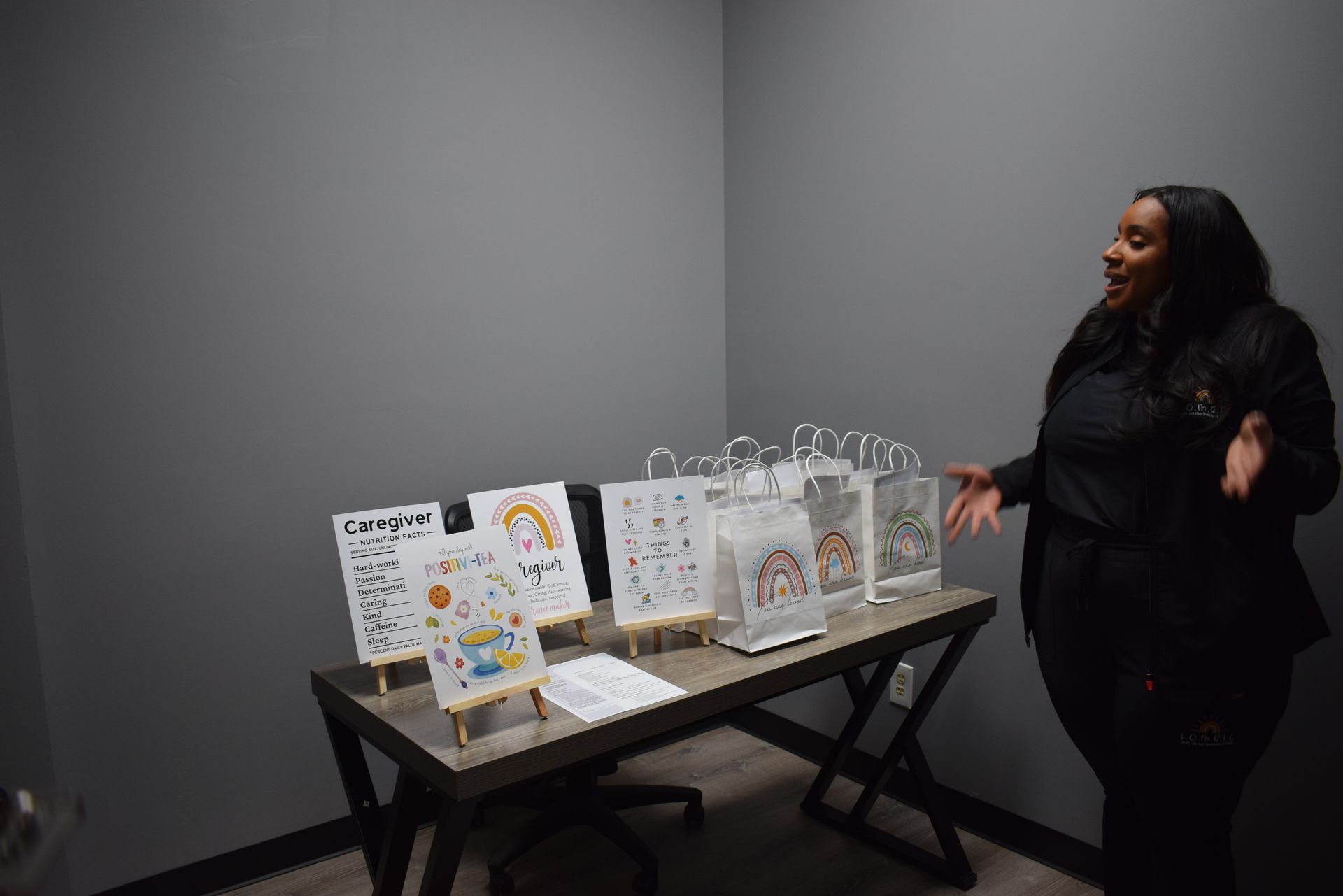 Woman in black standing beside a table of display bags and printed materials in a gray room