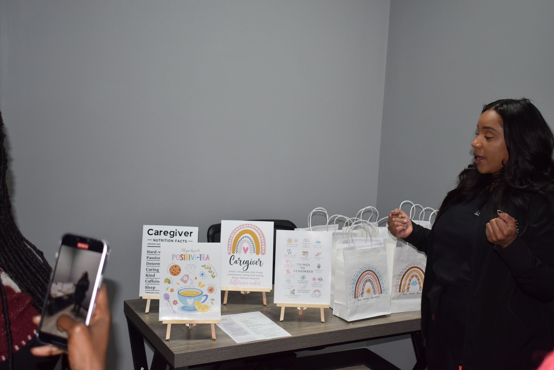 Woman presenting display boards and drawings on a table in a gray-walled room.