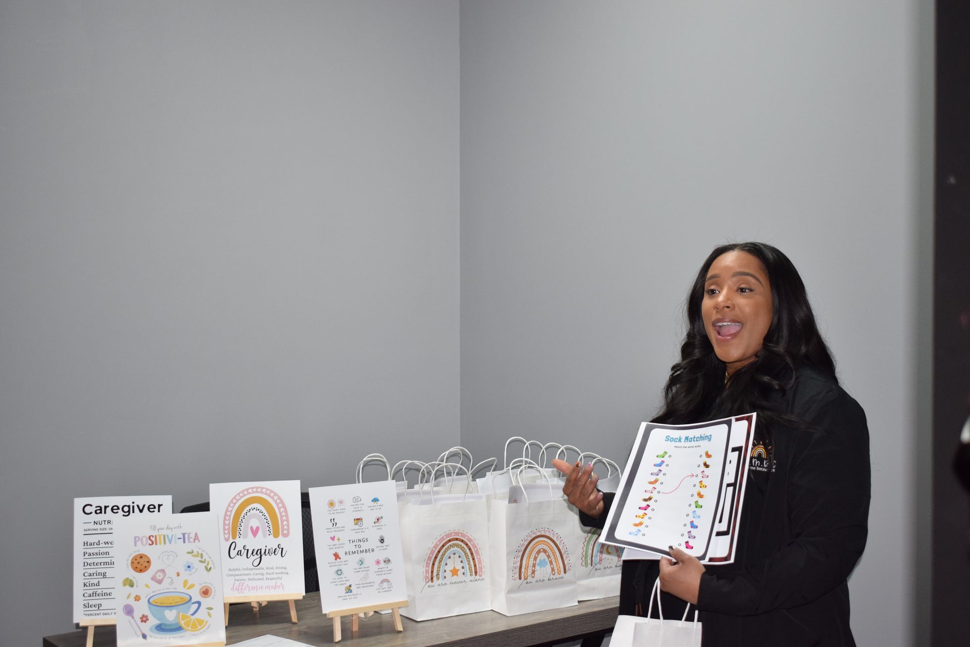 Woman presenting colorful posters and gift bags at a display table in a gray room