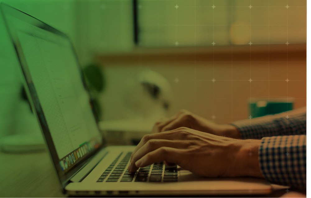 Hands typing on a laptop at a desk in a softly lit office, with a green-tinted screen.