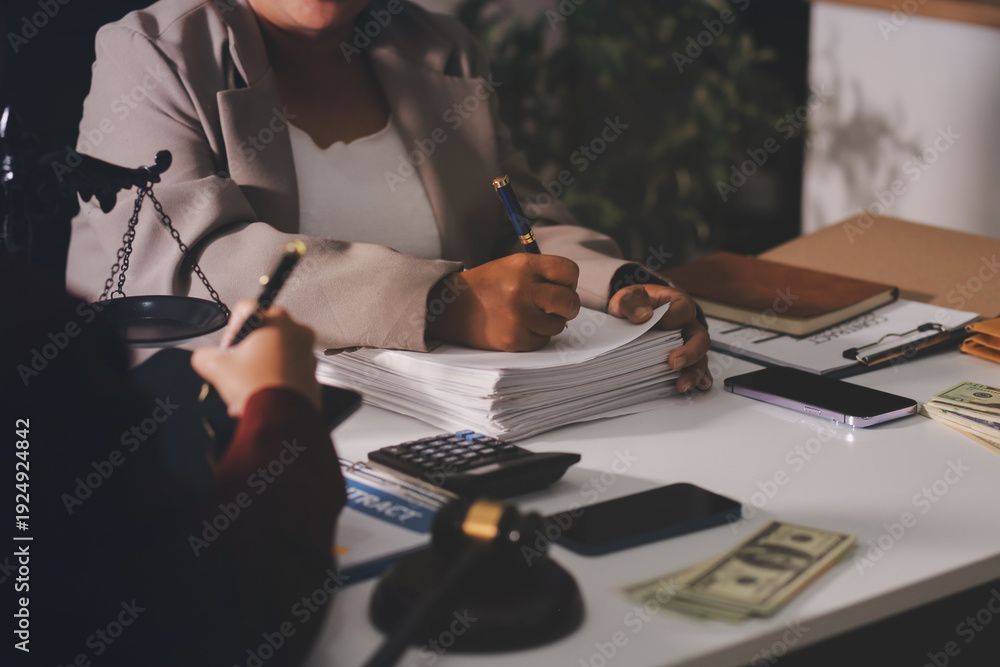 People signing documents at a desk with a laptop, papers, money, and a microphone