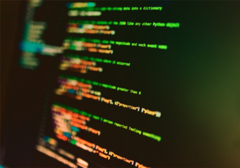 Blurred colorful computer code on a dark screen, glowing green, orange, and blue lines.