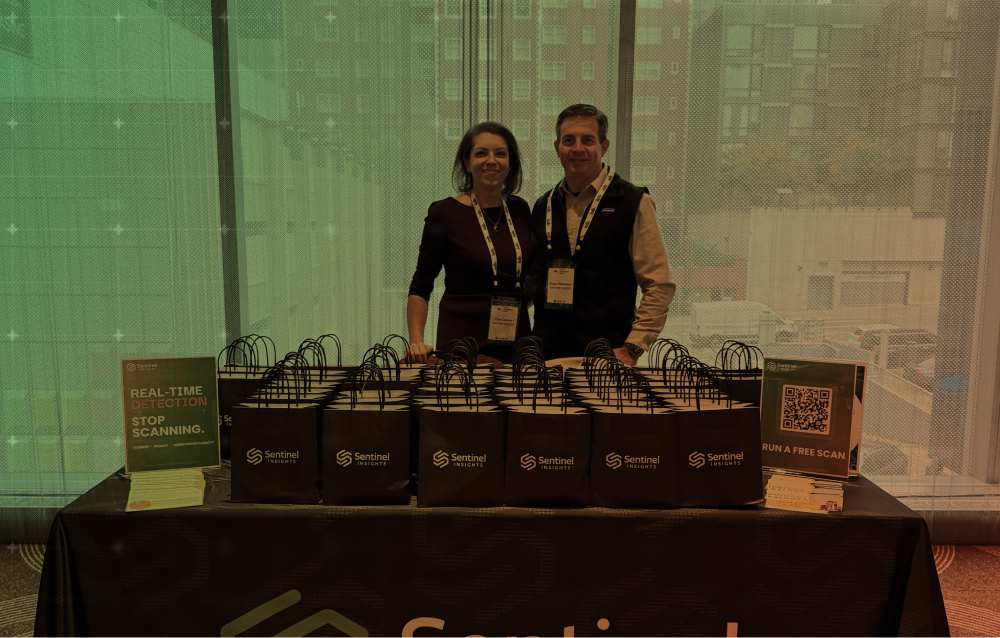 Two people behind a table of gift bags at a booth with a city skyline backdrop