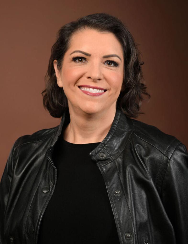 Smiling woman in a black leather jacket against a brown studio backdrop
