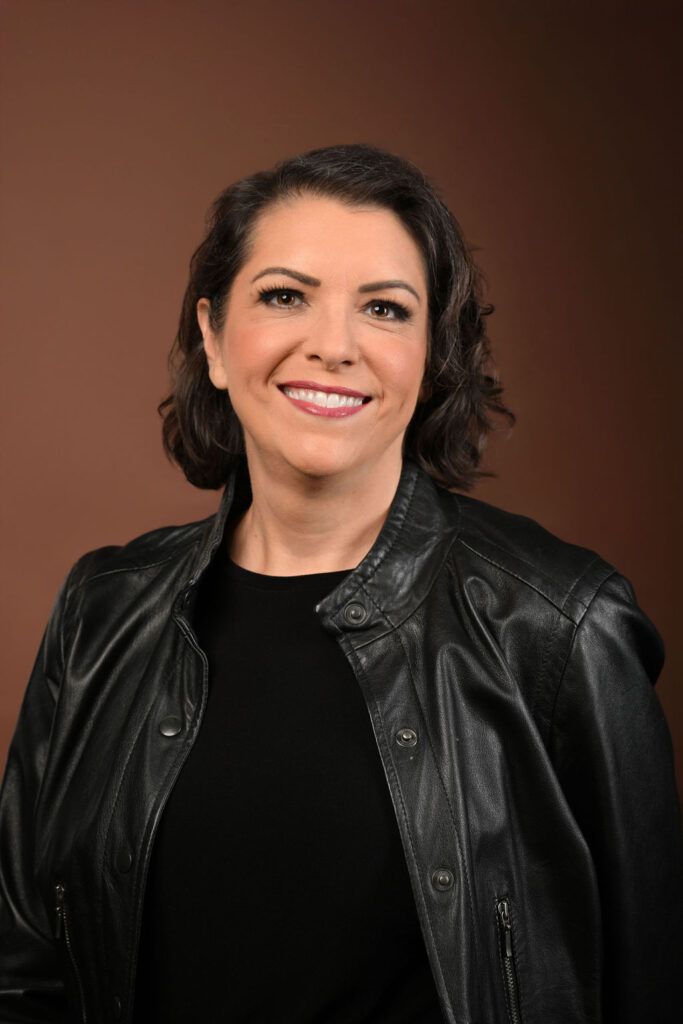 Smiling person in a black leather jacket against a warm brown studio backdrop