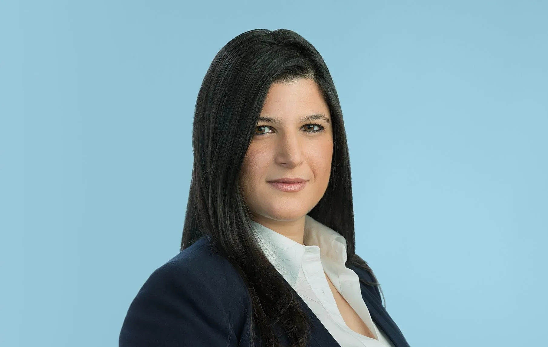 Portrait of a woman in a dark blazer and white shirt against a light blue background