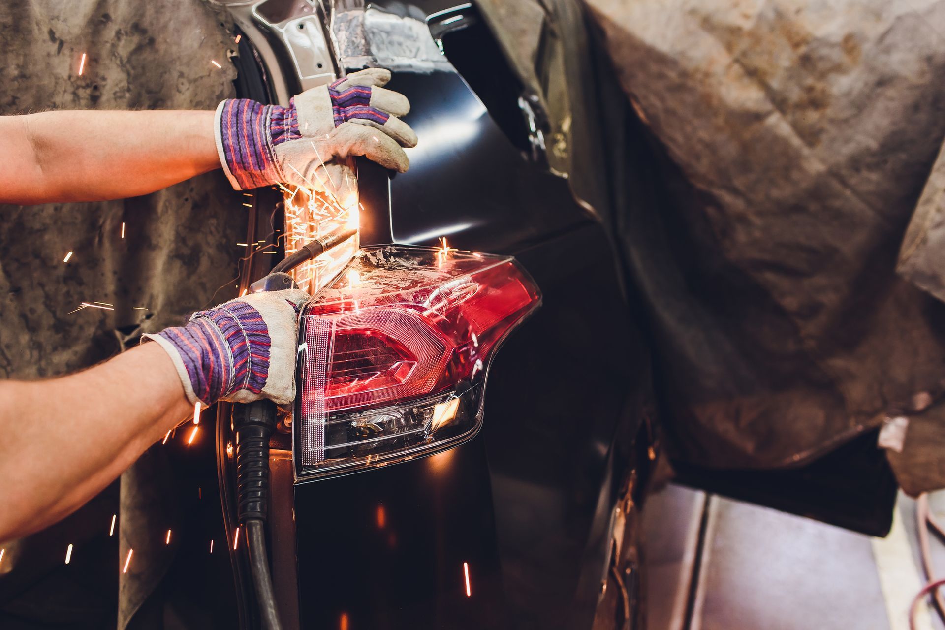 Welder using a torch on black metal, sparks flying, wearing gloves, in a workshop.