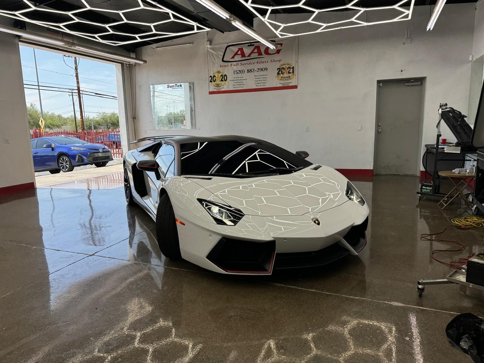White Lamborghini Aventador inside a garage with a blue car visible through an open door.