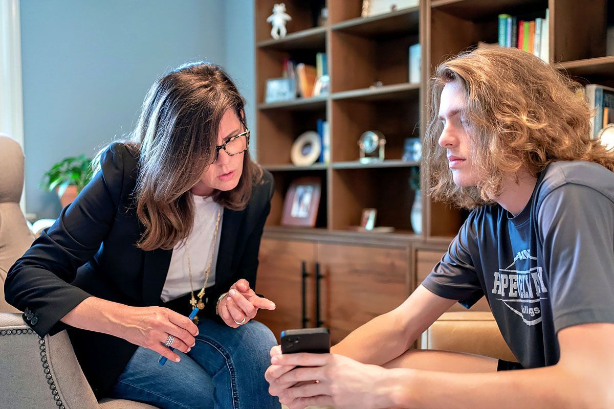 Two people leaning over a phone in a cozy room with shelves in the background