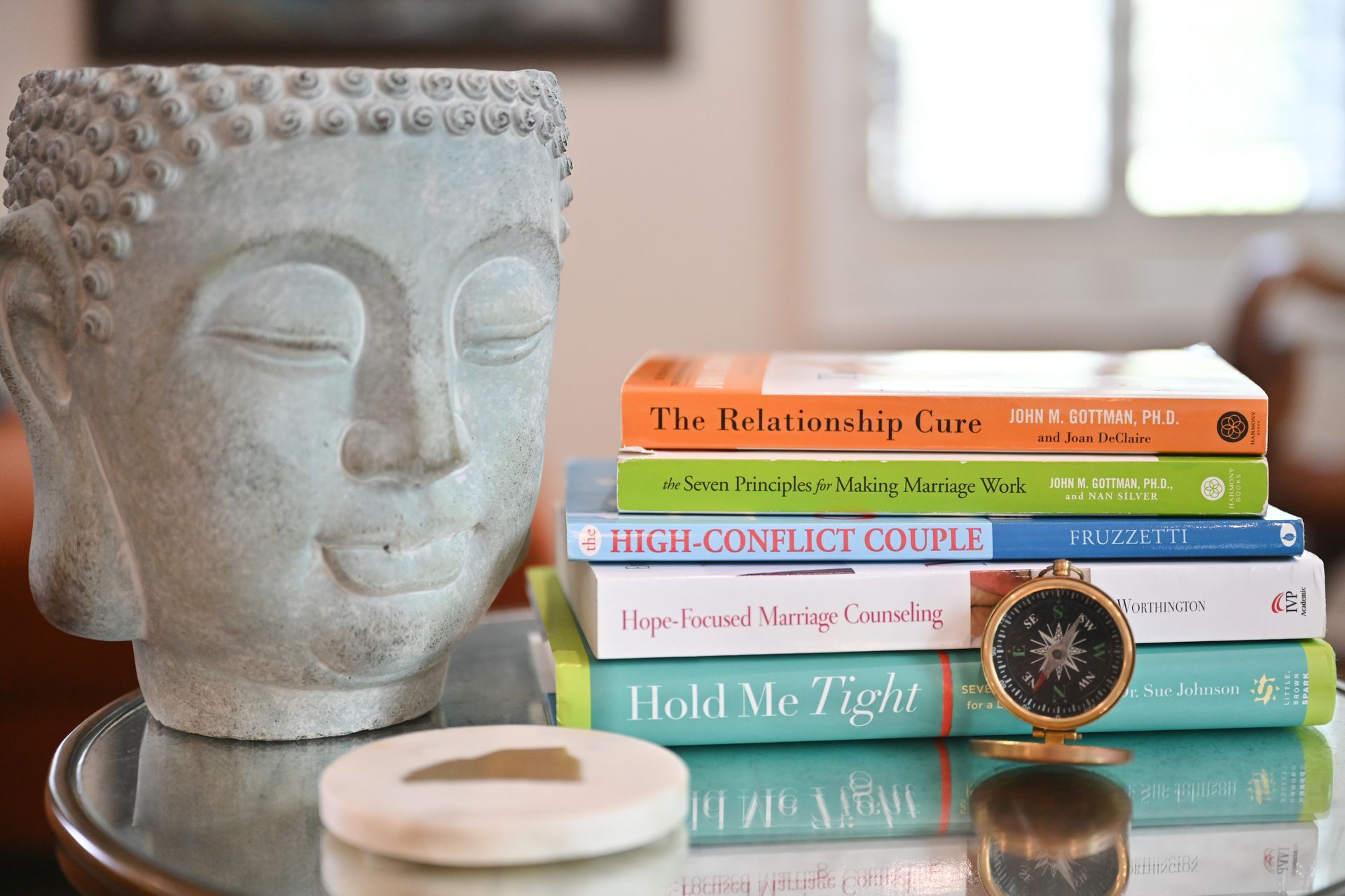 Stack of self-help books beside a Buddha statue and a candle on a table.