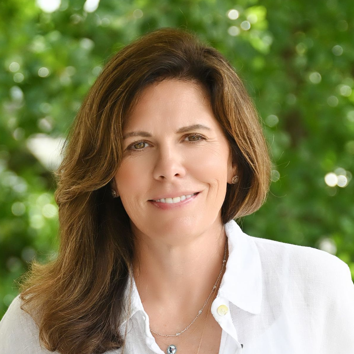 Smiling woman in a white blouse outdoors with blurred green foliage background