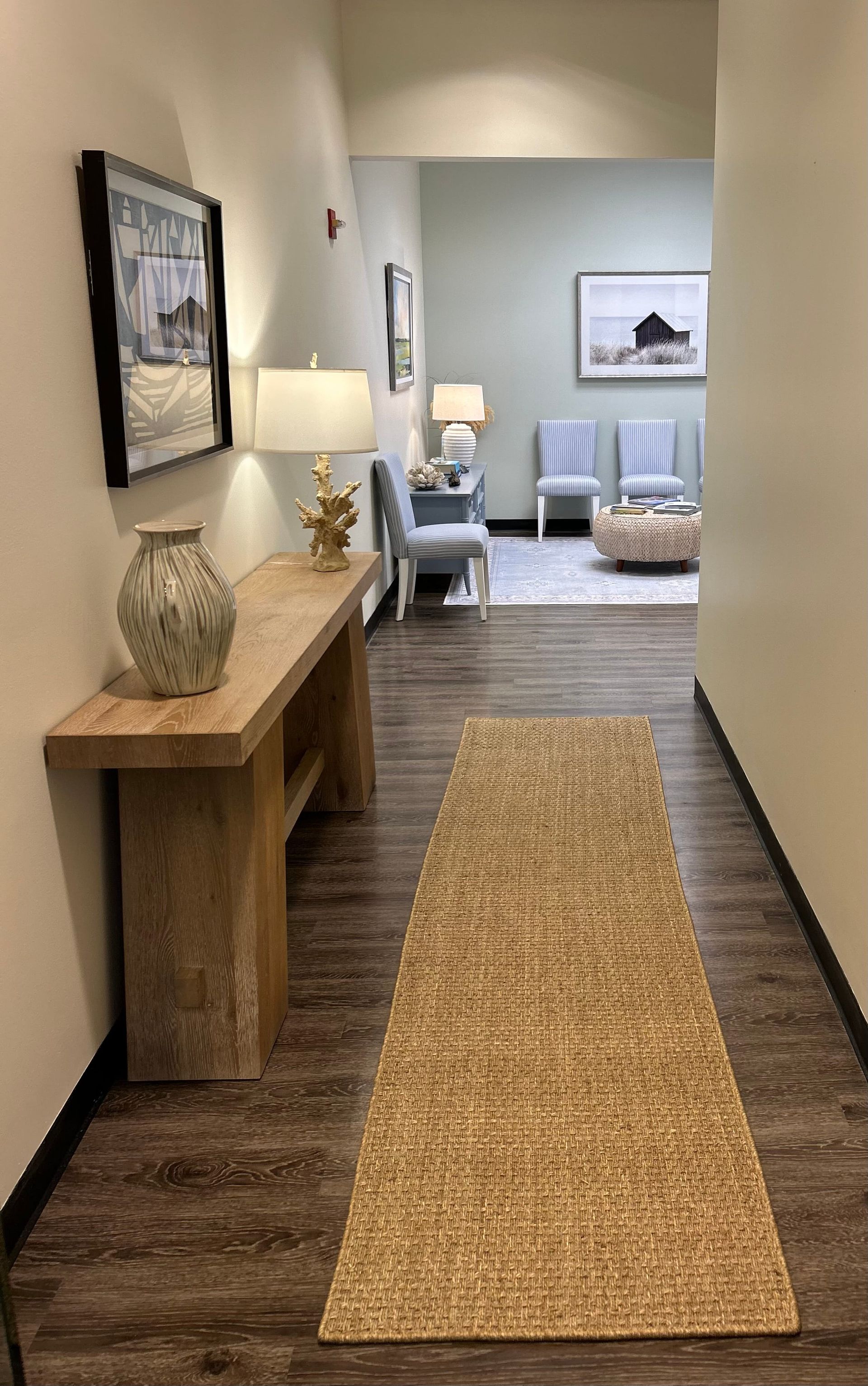 Narrow hallway with a woven runner, console table, framed art, and a cozy seating area in the background.