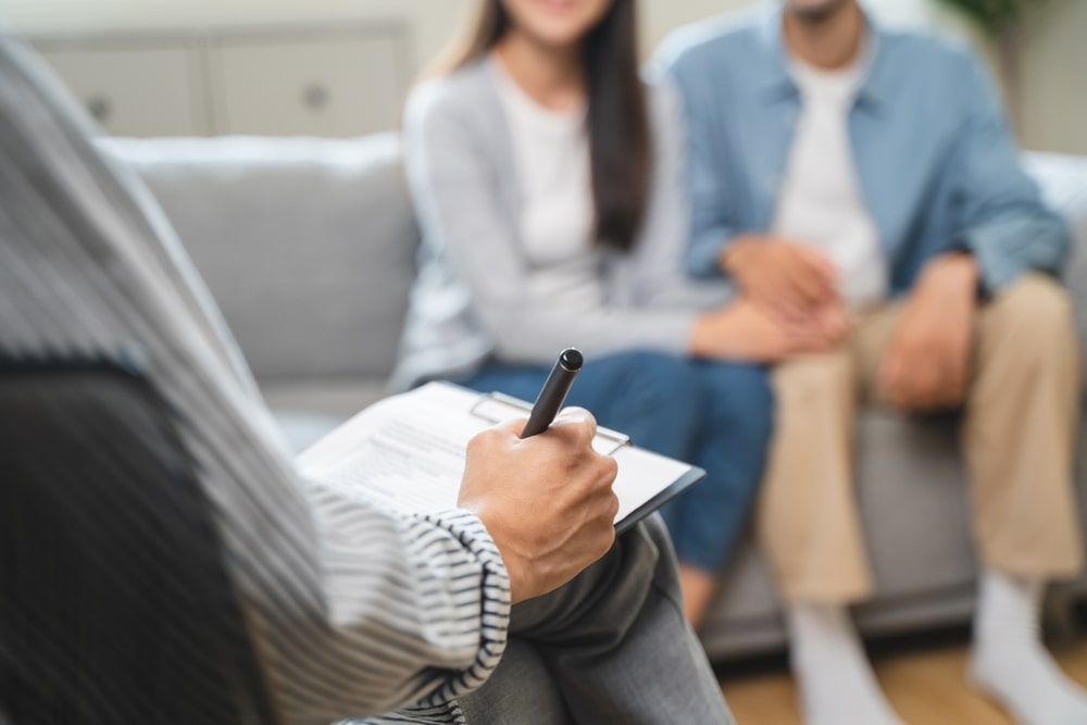 Therapist taking notes while a blurred couple sits on a couch during counseling session
