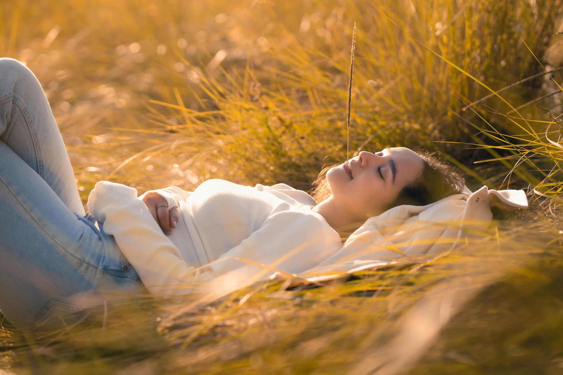 Person lying in tall golden grass, resting with eyes closed in warm sunlight.