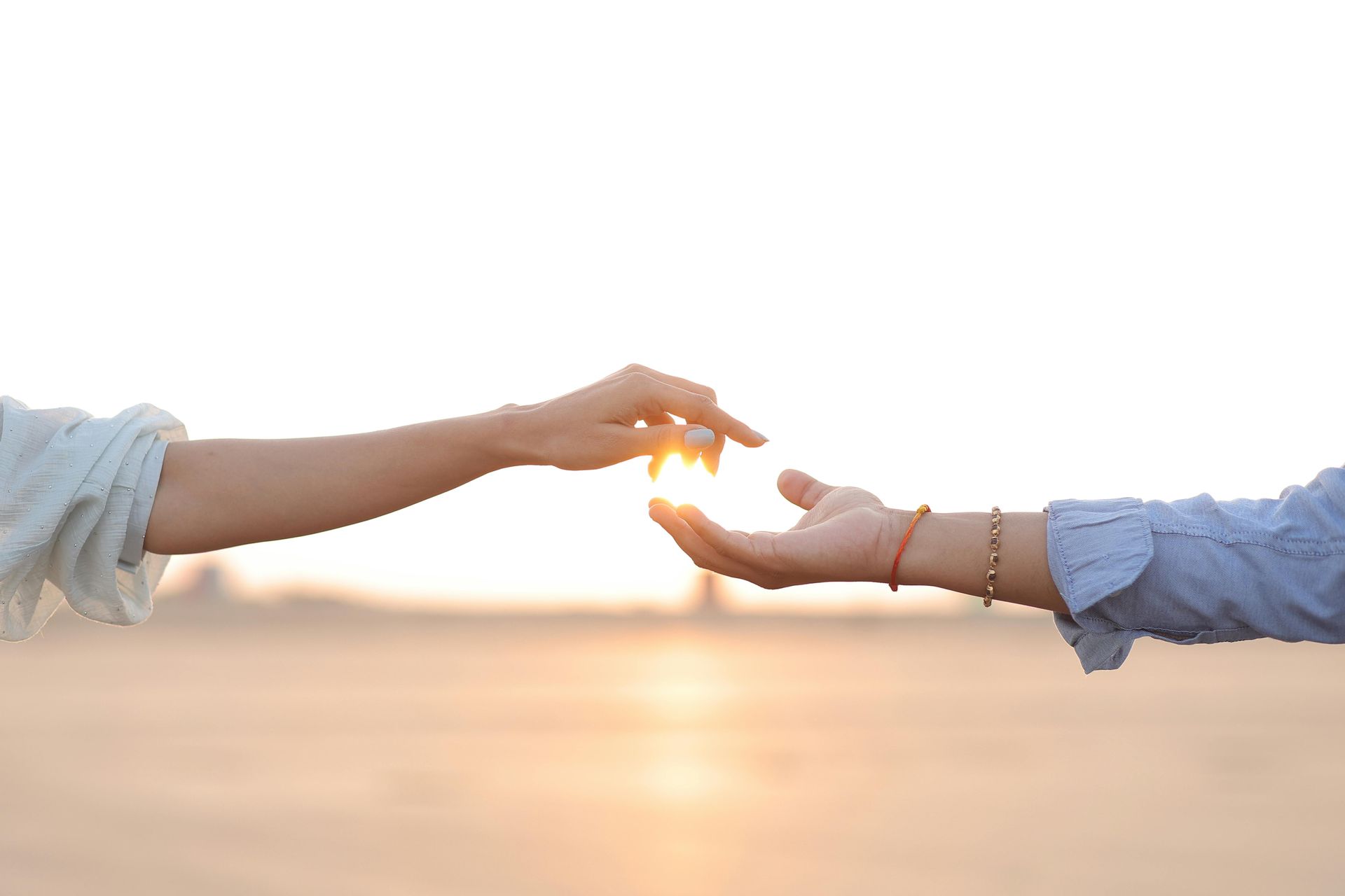 Two hands reaching toward each other at sunset over a beach