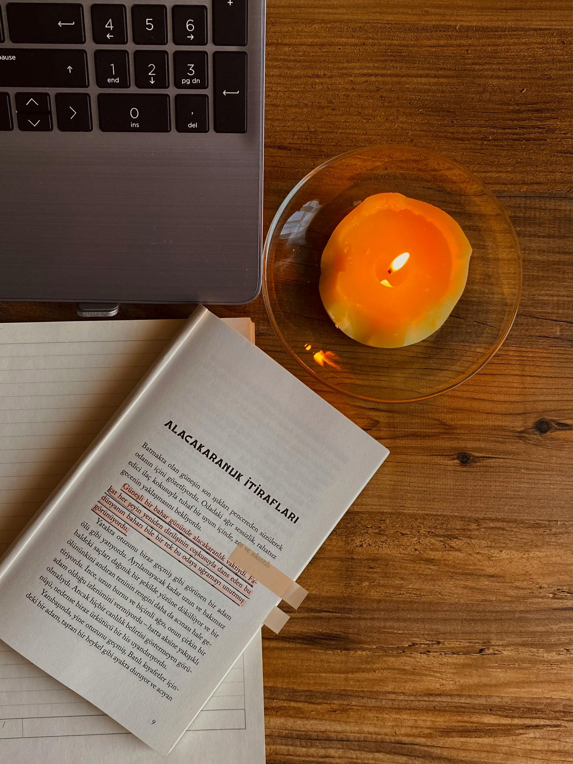 Laptop beside an open book and a glass bowl holding an egg on a wooden desk.