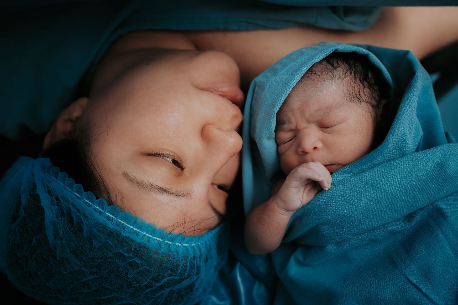 Two sleeping newborns swaddled in blue blankets, lying close together and touching foreheads.