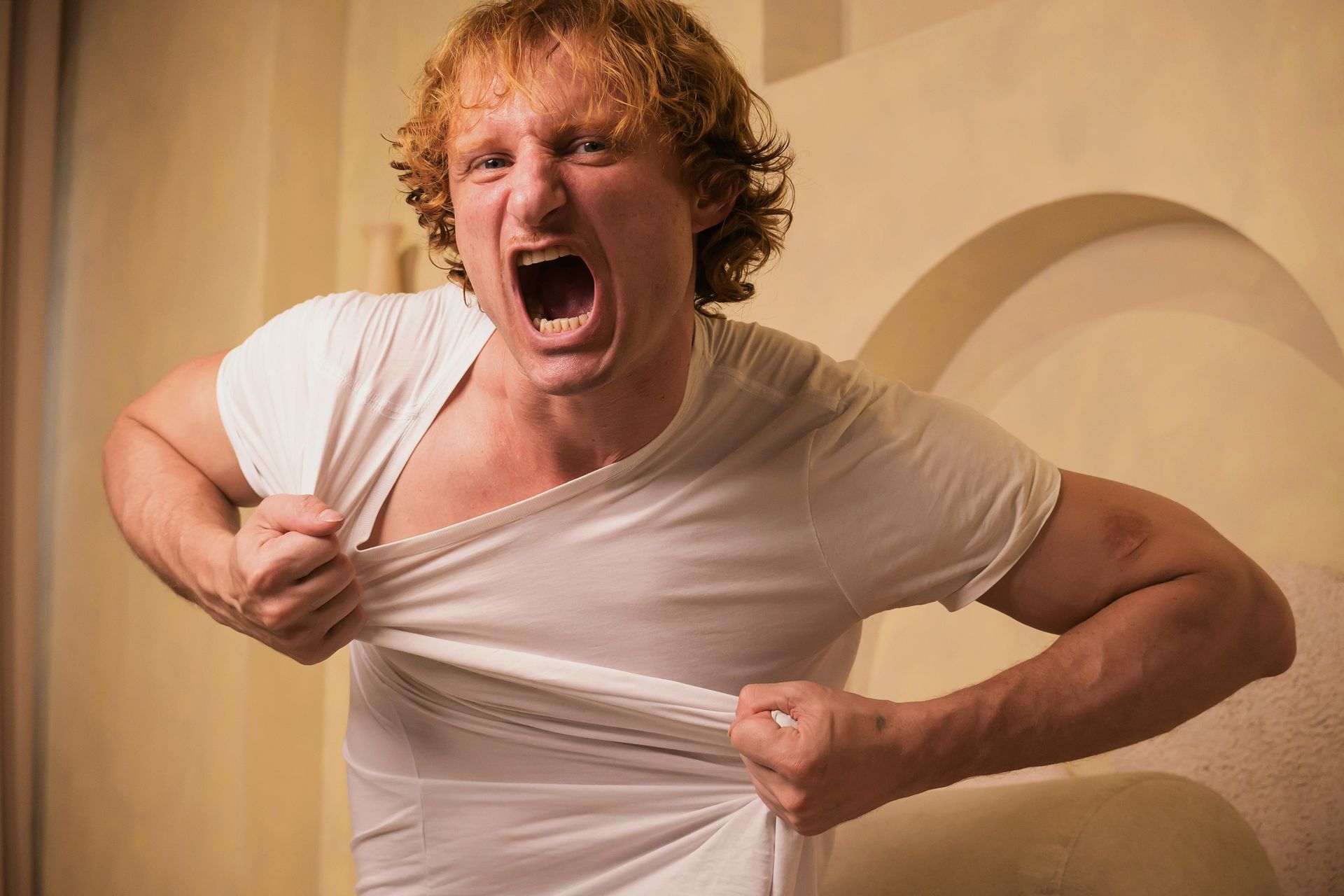Angry person in a white T-shirt tearing it apart indoors