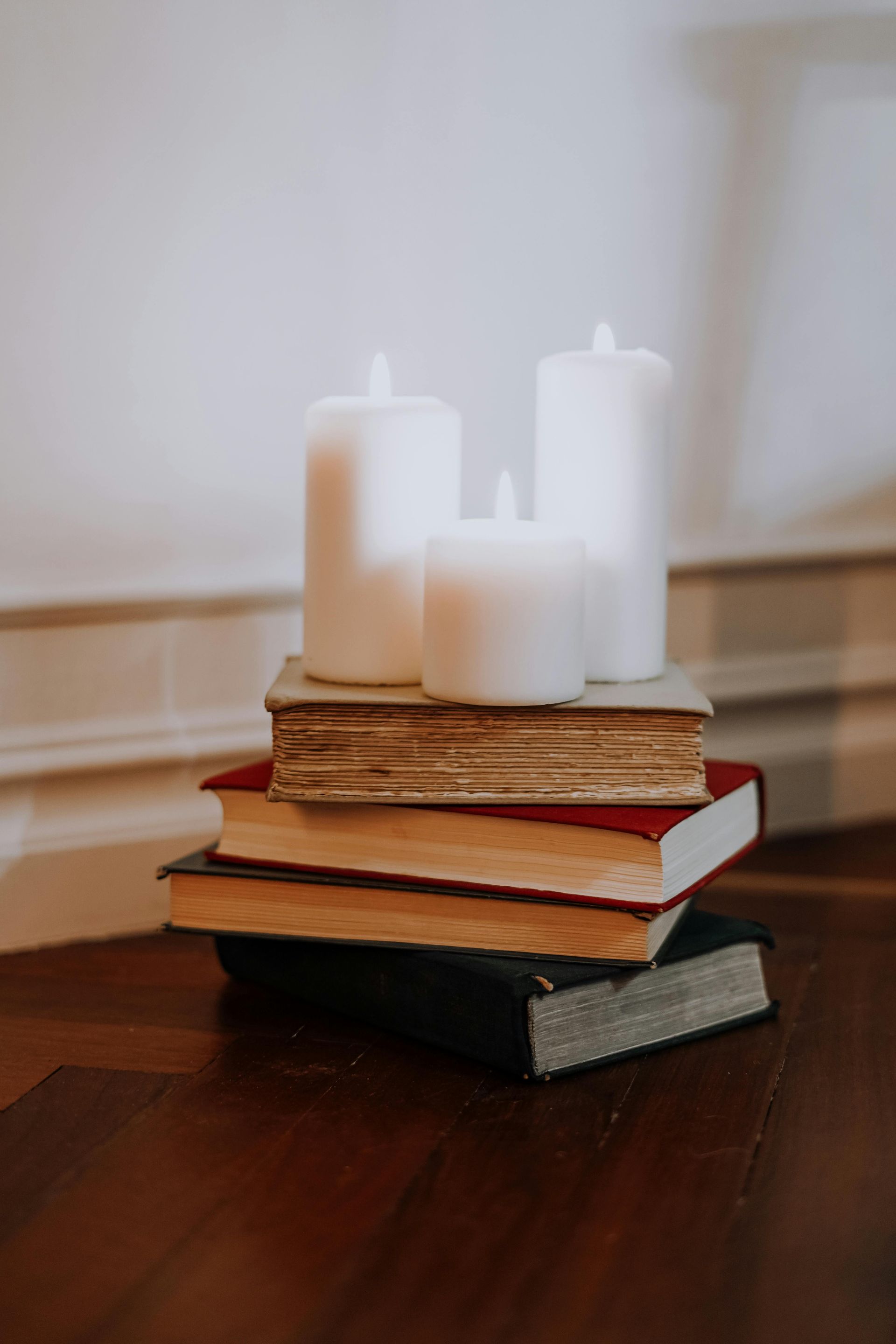 Stack of books topped with white pillar candles on a wooden table in a soft-lit room