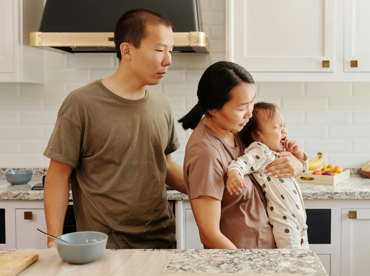Family in a bright kitchen, one adult holding a baby while another adult stands nearby.