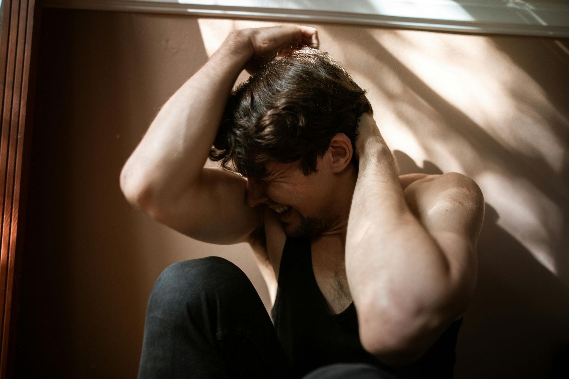 Person sitting on the floor with hands in hair, looking down in a dim, warm-lit room