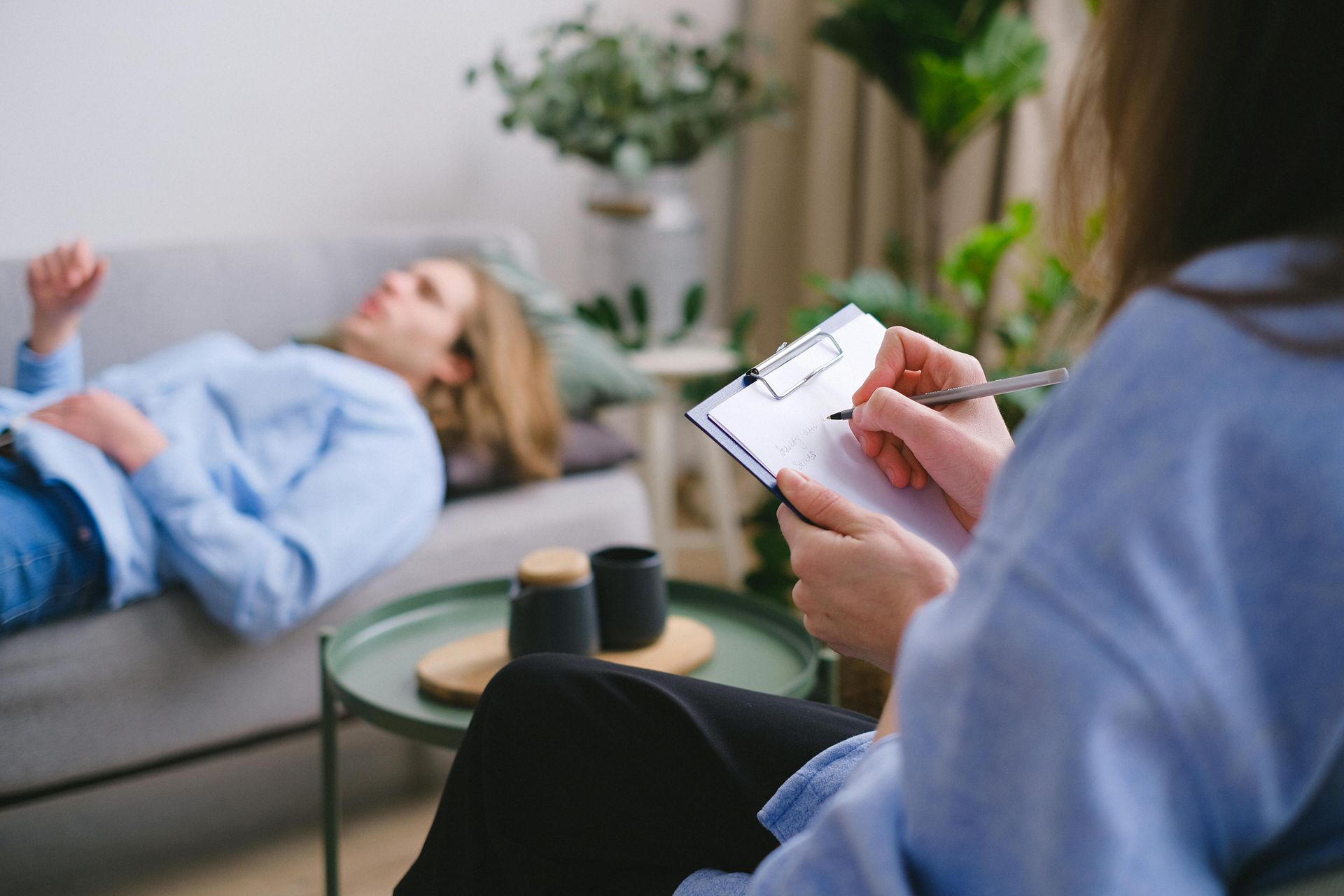 Therapist taking notes while client lies on a sofa in a bright counseling room
