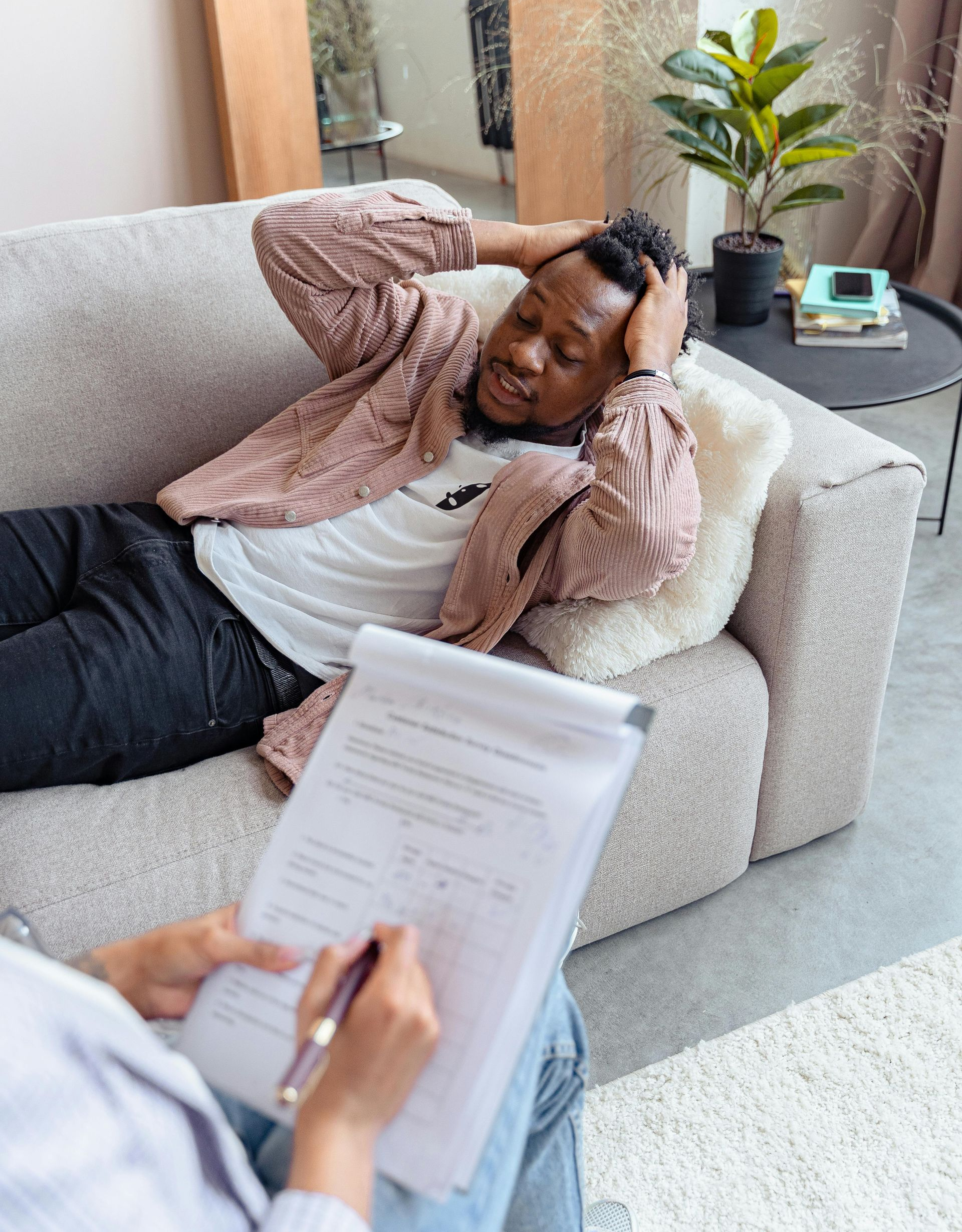 Person reclining on a couch during a therapy session, holding their head while a clipboard is in the foreground