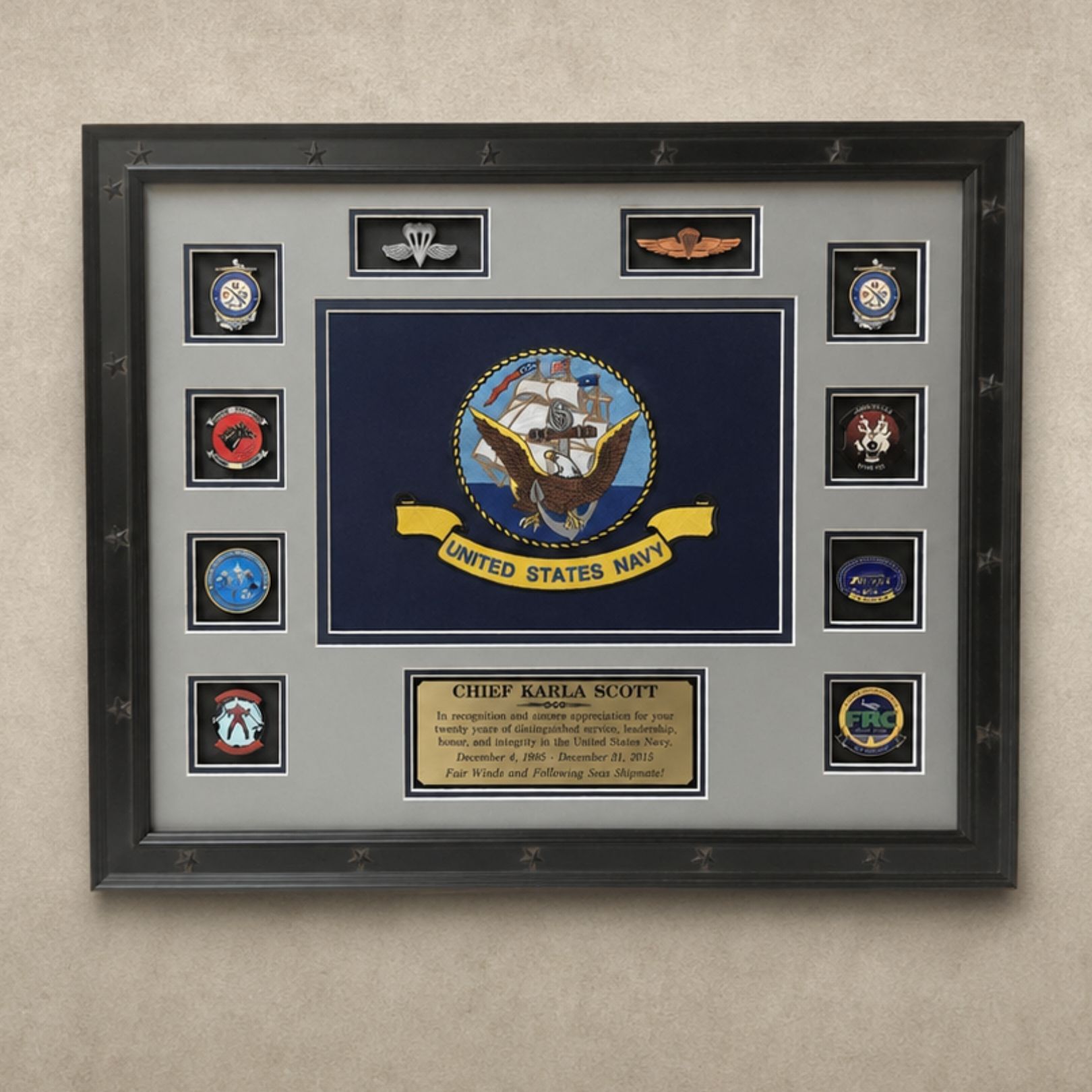 Framed U.S. Navy shadow box with insignia patches and a central plaque on a gray background