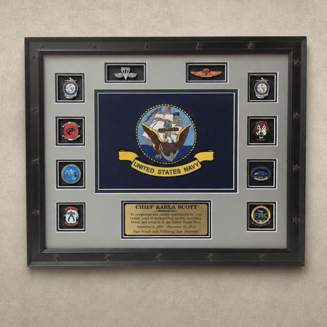 Framed U.S. Navy shadow box with insignia patches and a central plaque on a gray background