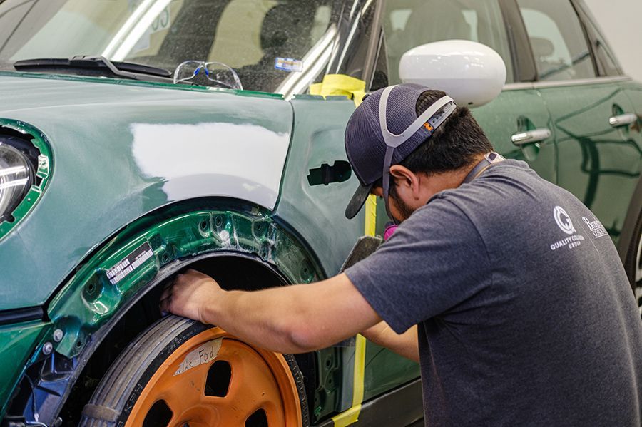 Mechanic repairing a green car’s front wheel arch with orange rim in a workshop