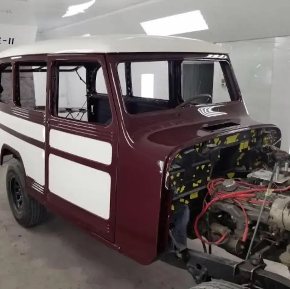 A two-toned maroon and white vintage station wagon body undergoing restoration inside a paint booth.