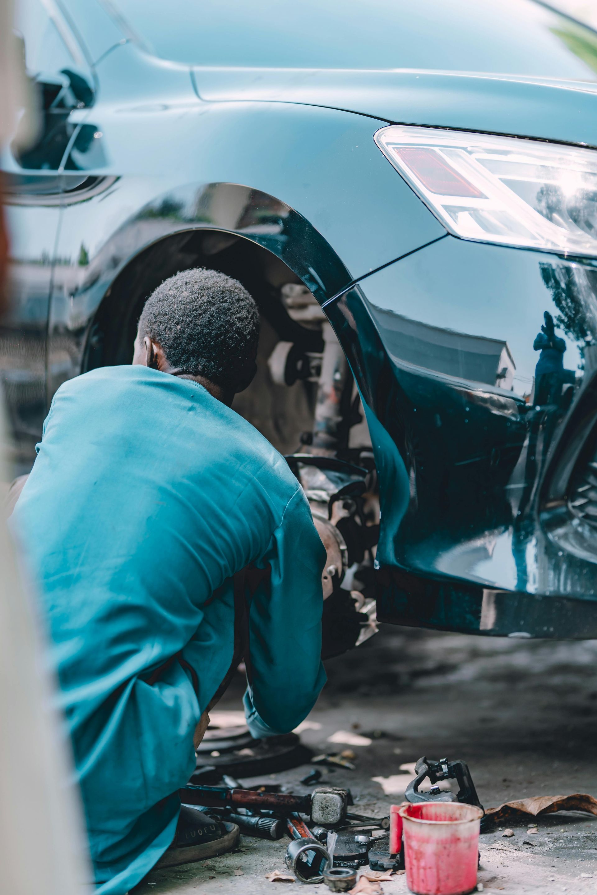 Mechanic repairing a dented blue car bumper with tools on the ground