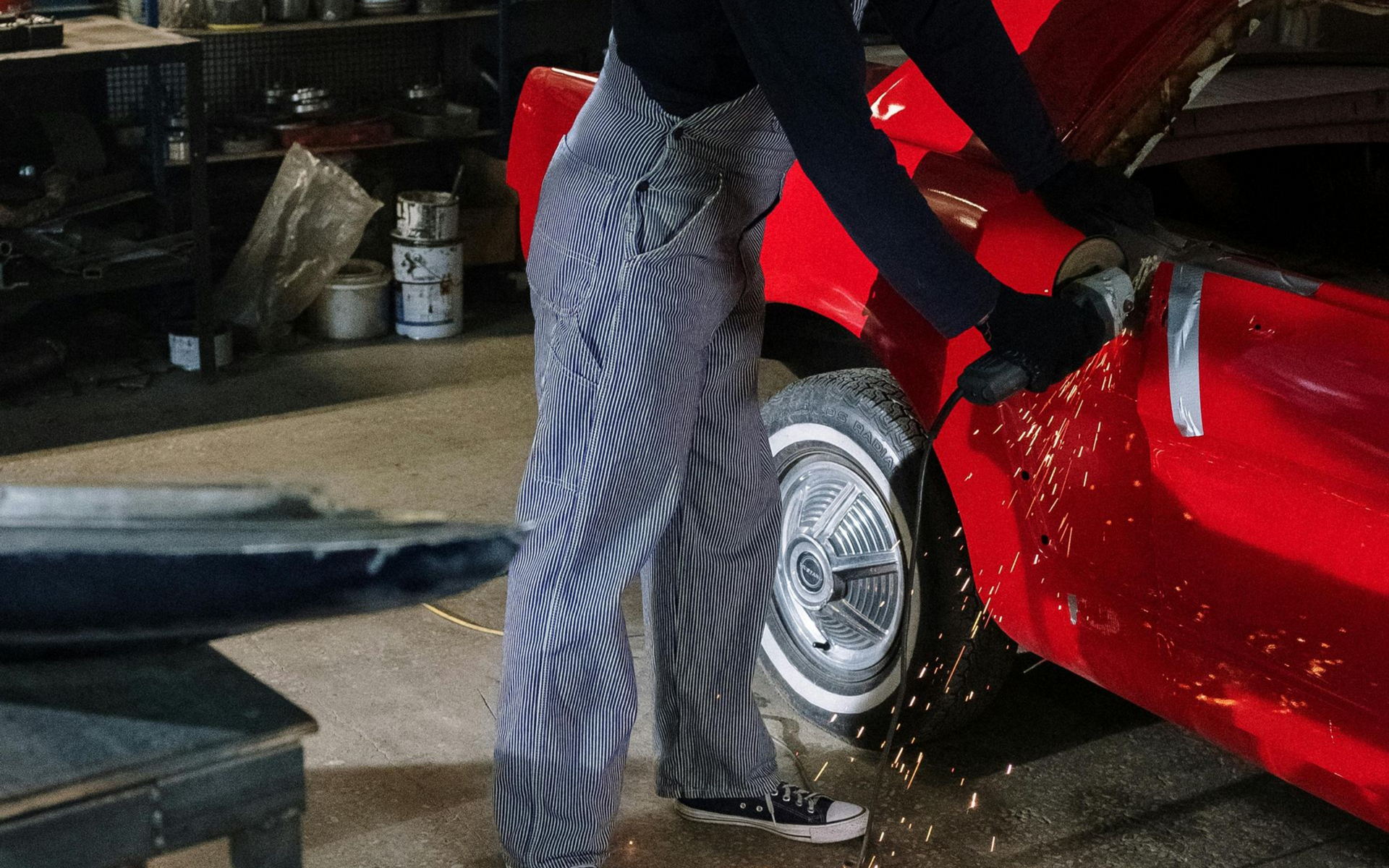 Person cleaning a red car wheel with water spraying in a garage